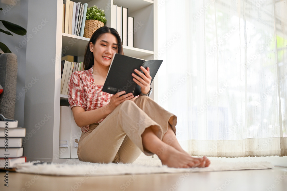 Charming Asian woman relaxes reading a book on the living room's floor. Charming Asian woman relaxes reading a book on the living room's floor.