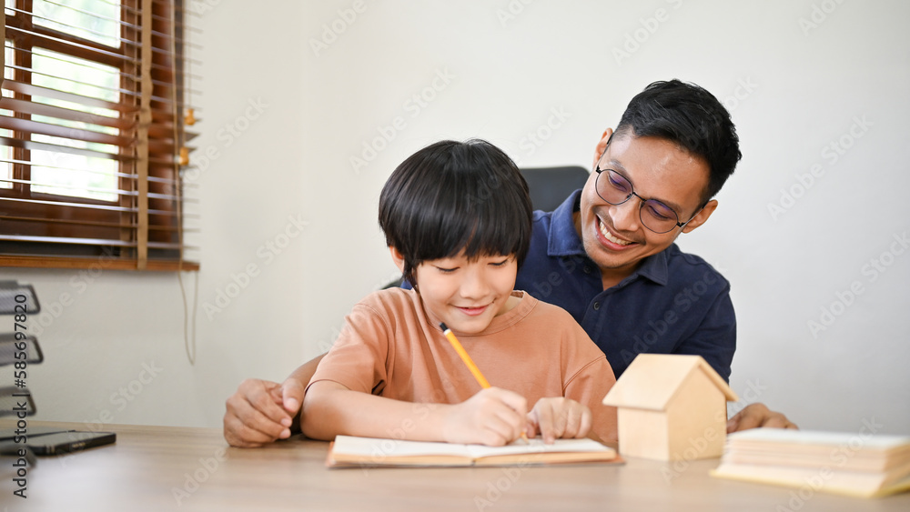 A caring Asian father teaching his son to write the alphabet on a paper. A caring Asian father teaching his son to write the alphabet on a paper.