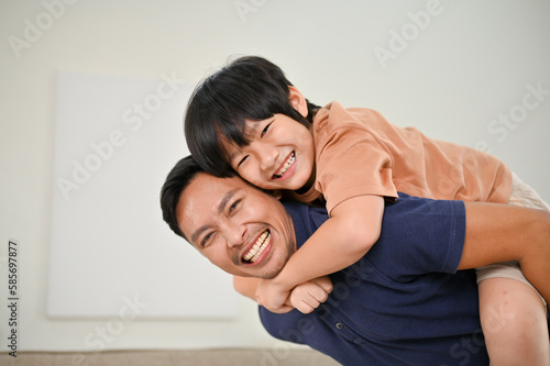 Happy Asian son and dad having a fun time together at home, playing and piggybacking