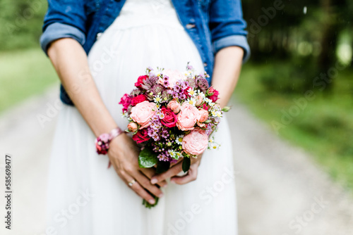 Schwangere Braut mit Brautstrauss im Brautkleid und Jeansjacke