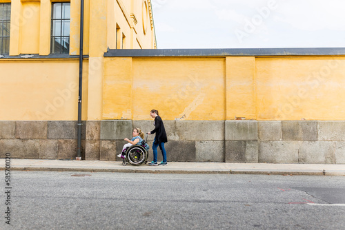 Assistant helping disabled woman in wheelchair move around city