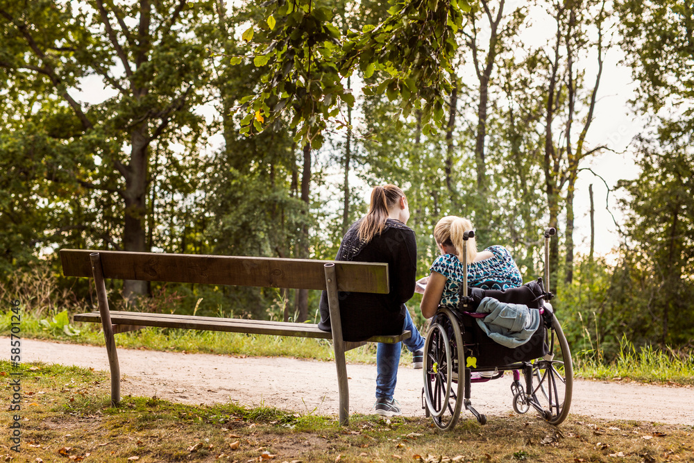 Disabled woman in wheelchair with assistant in park Disabled woman in wheelchair with assistant in park