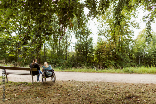 Disabled woman in wheelchair with assistant in park