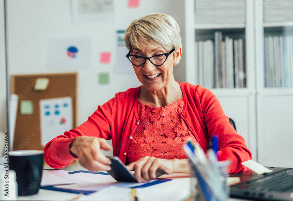 Happy senior woman using mobile phone while working at home with laptop Happy senior woman using mobile phone while working at home with laptop