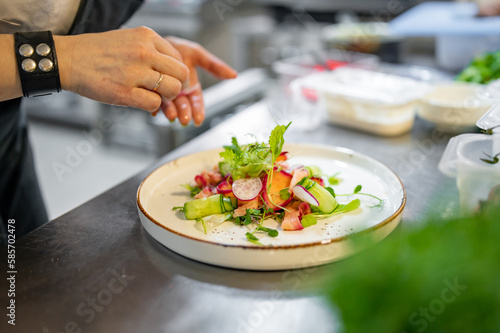 Chef cooking Green salad with salmon, cucumbers, lettuce, spices, caviar on restaurant kitchen