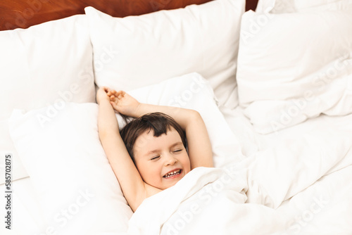 Little boy lying and stretching his arms in the bed at home in the morning. Home lifestyle boy relaxing sleeping on bed in bedroom.
