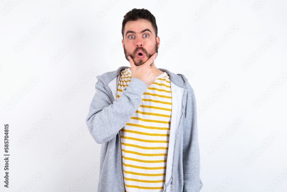 Young caucasian mán wearing trendy clothes over white background Looking fascinated with disbelief, surprise and amazed expression with hands on chin Young caucasian mán wearing trendy clothes over white background Looking fascinated with disbelief, surprise and amazed expression with hands on chin