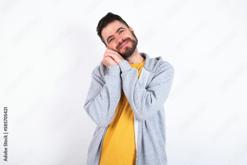 Charming serious Young caucasian mán wearing trendy clothes over white background keeps hands near face smiles tenderly at camera Charming serious Young caucasian mán wearing trendy clothes over white background keeps hands near face smiles tenderly at camera