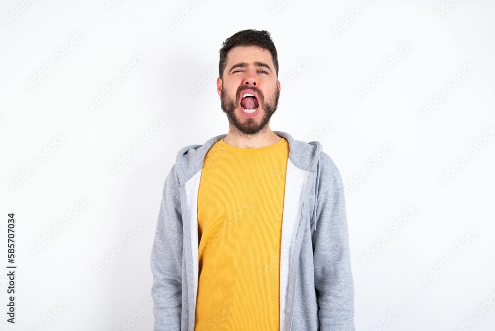 Young caucasian mán wearing trendy clothes over white background yawns with opened mouth stands. Daily morning routine Young caucasian mán wearing trendy clothes over white background yawns with opened mouth stands. Daily morning routine