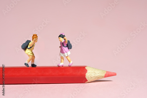 Miniature tiny people toys photography. Two kids standing above red pencil. Isolated on pink background.