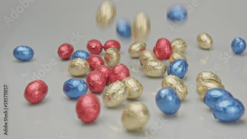 Wide view of a lot of chocolate Easter eggs falling on a white studio background in slow motion photo