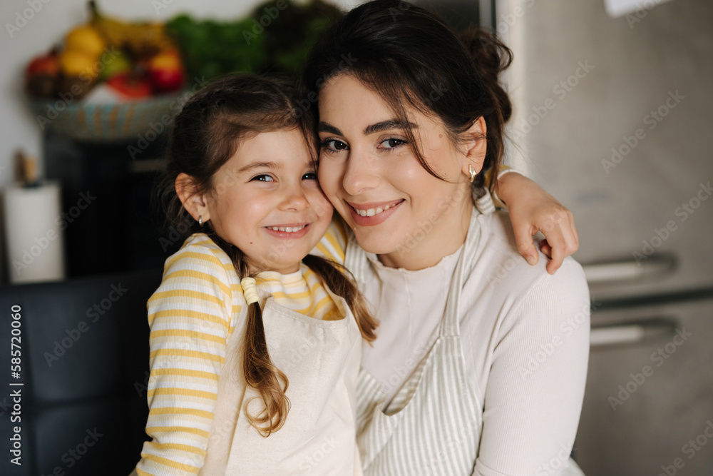 Close-up portrait of daughter with mom on kitchen. Beautiful girls dressed in apron Close-up portrait of daughter with mom on kitchen. Beautiful girls dressed in apron