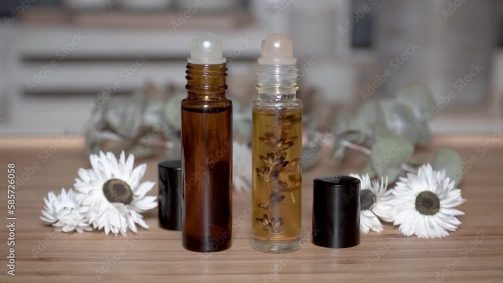 Two liquid cosmetics in roll on transparent and amber glass bottle at wooden background with white flowers and dry lavender bunch. Two liquid cosmetics in roll on transparent and amber glass bottle at wooden background with white flowers and dry lavender bunch.