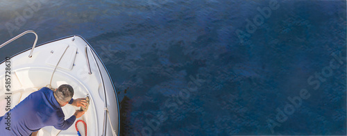 A male sailor washes a white boat. Yacht maintenance concept. Summer banner on the sea.