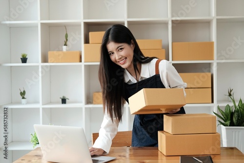 Portrait businesswoman smiling and holding tablet working at home. Asian woman is owner small business online with shipping box. Concept new normal. © Sucharat
