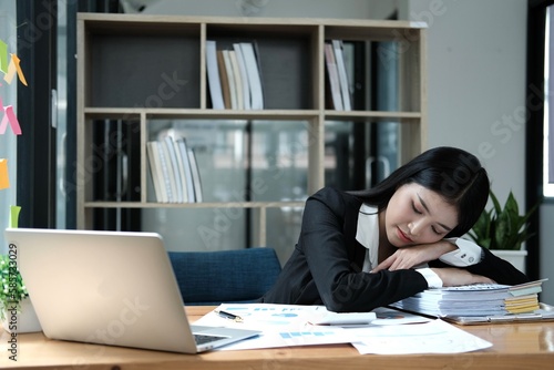 Tired businesswoman sleeping with document on the desk at office. Overwork, working overtime and stress at work concept. photo