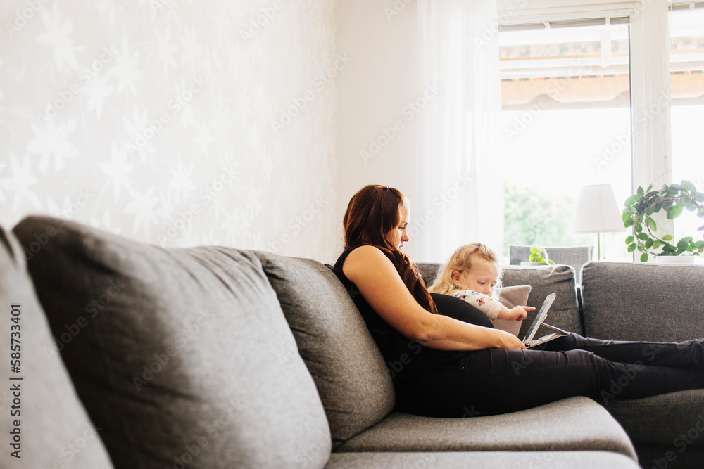 Pregnant woman with daughter (2-3) on sofa using tablet Pregnant woman with daughter (2-3) on sofa using tablet