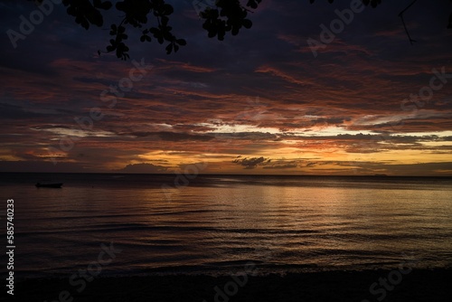 Picturesque sunset on the beach of Siquijor in the Philippines  the cloudy sky shines in golden yellow orange and red colors  in the foreground treetops.