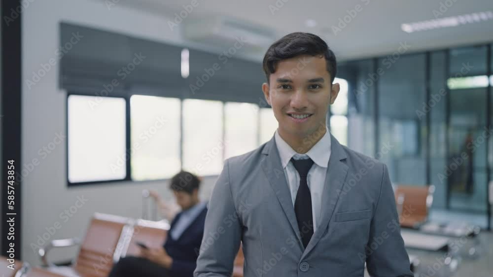 Asian businessman passenger wearing suit smiling and standing in airport terminal to boarding gate waiting for flight looking at camera Asian businessman passenger wearing suit smiling and standing in airport terminal to boarding gate waiting for flight looking at camera