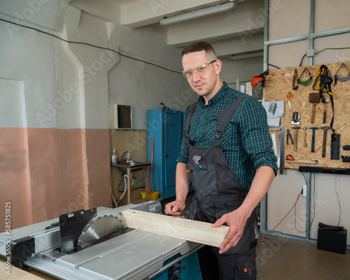 The carpenter cuts a wooden board on a circular machine.