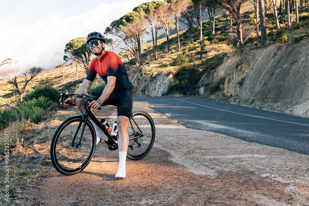 Smiling cyclist standing on a roadside in wild terrain. Male bike rider ...