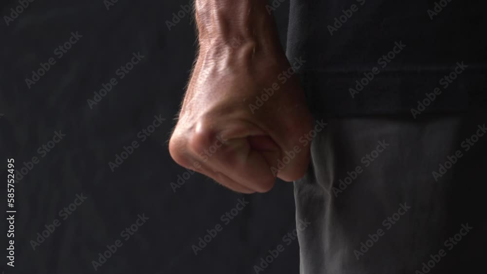 Close-up of palm of an mature man with bulging veins is tightly clenched into a fist in rage on a black background. Consept aggression and ready to fight.