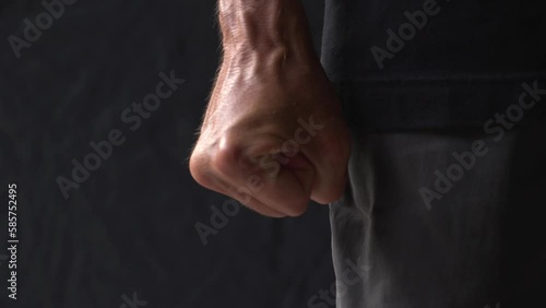 Close-up of palm of an mature man with bulging veins is tightly clenched into a fist in rage on a black background. Consept aggression and ready to fight.