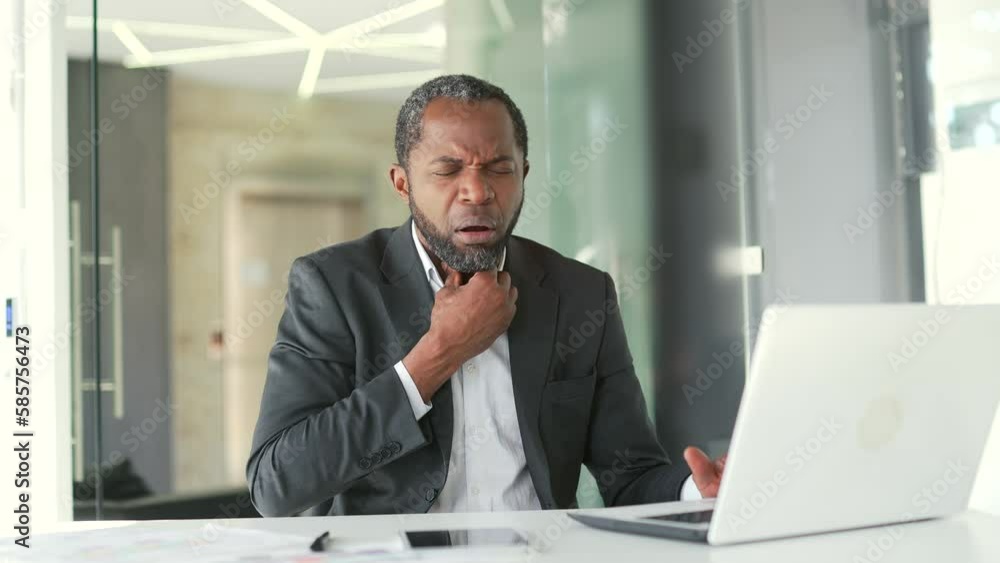 A mature african american man in a formal suit is suffering from a sore throat while sitting at a desk at a workplace in a modern office. A sad middle aged male is massaging a sore spot with his hands A mature african american man in a formal suit is suffering from a sore throat while sitting at a desk at a workplace in a modern office. A sad middle aged male is massaging a sore spot with his hands