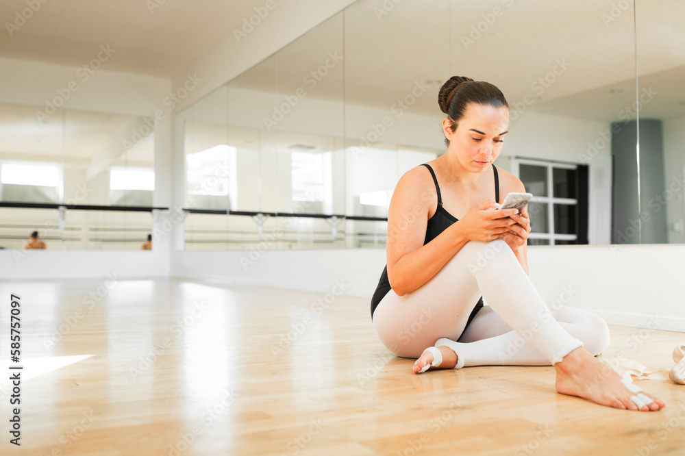 Ballerina sitting on wooden floor and using smart phone Ballerina sitting on wooden floor and using smart phone