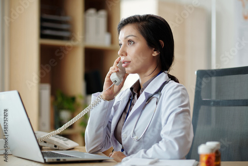 Wallpaper Mural Physician answering phone call from patient when working at office desk Torontodigital.ca