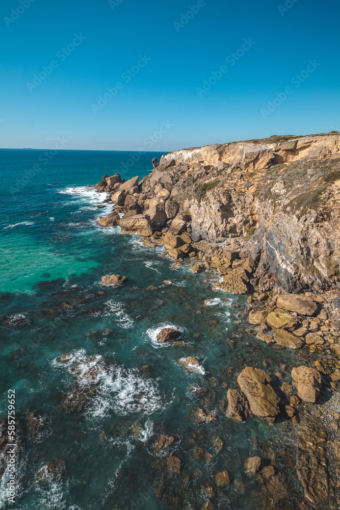 Breathtaking cliffs with crashing waves in the afternoon sun on the Atlantic coast near Vila Nova de Milfontes, Odemira, Portugal. In the footsteps of Rota Vicentina. Fisherman trail. Clear blue sky