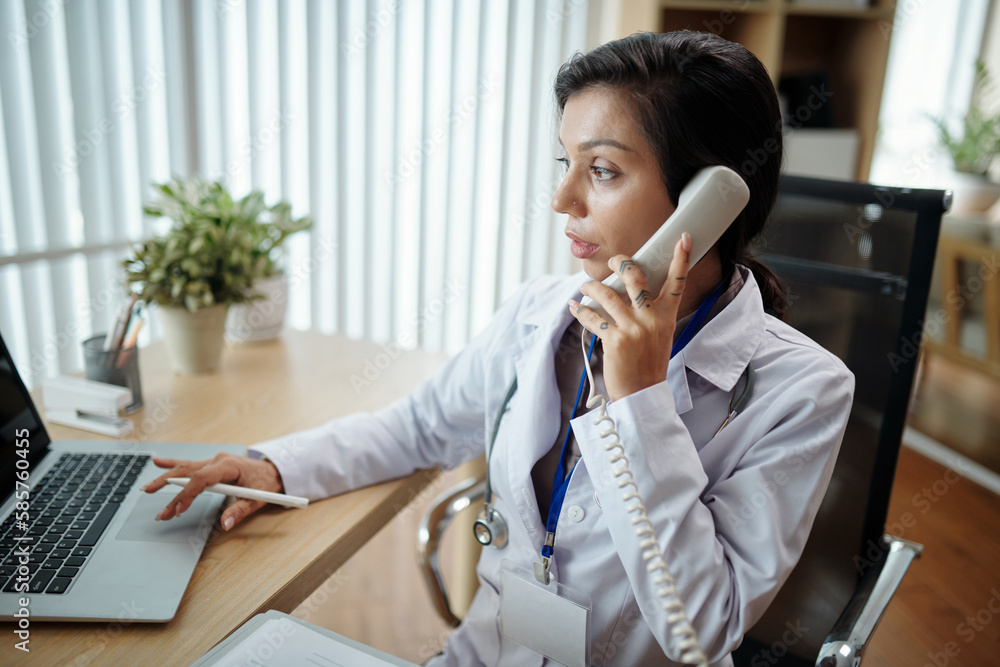 Head of clinic talking on phone with medical nurse when checking schedule of doctors Head of clinic talking on phone with medical nurse when checking schedule of doctors