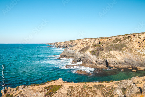 Breathtaking cliffs with crashing waves in the afternoon sun on the Atlantic coast near Vila Nova de Milfontes, Odemira, Portugal. In the footsteps of Rota Vicentina. Fisherman trail. Clear blue sky © Fauren