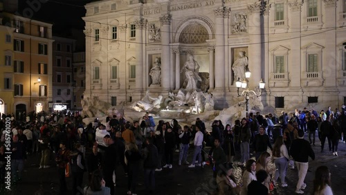 The pedestrian area of the Trevi fountain crowded with citizens and tourists strolling on a Sunday afternoon.