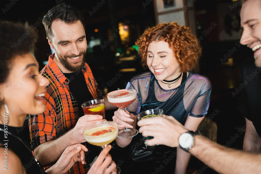 Overjoyed multiethnic friends toasting with different cold cocktails in bar.