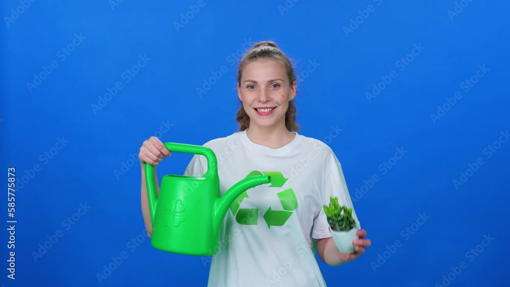 Ecology, woman ecologist, holding a watering can and a plant in his hands against a blue background, greening the planet. Ecology, woman ecologist, holding a watering can and a plant in his hands against a blue background, greening the planet.