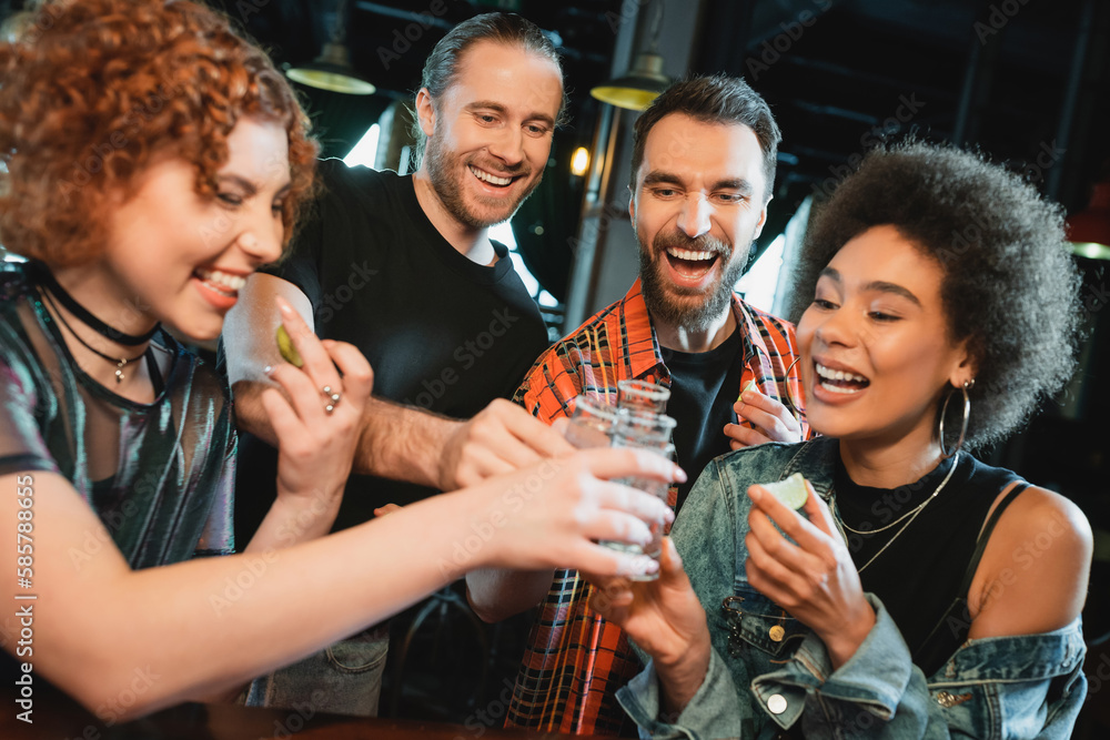 Carefree multiethnic friends holding lime and clinking tequila with salt in bar. Carefree multiethnic friends holding lime and clinking tequila with salt in bar.