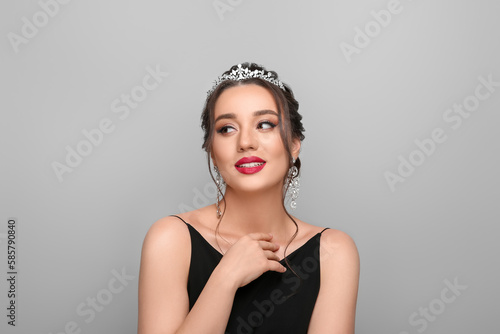 Beautiful young woman wearing luxurious tiara on light grey background