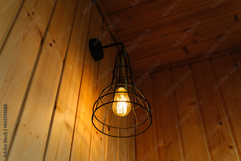 Stylish scandinavian composition of black bra with vintage edison lamp and wooden wall. Loft style in modern home decor.