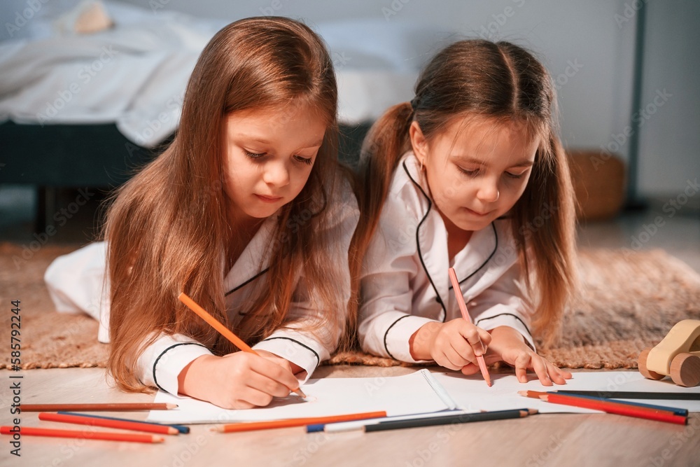 Drawing and lying down on the floor. Two little girls are playing and having fun together in domestic room Drawing and lying down on the floor. Two little girls are playing and having fun together in domestic room