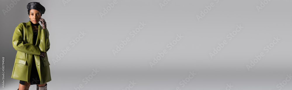 Fashionable african american model in leather beret and coat posing on grey, banner.