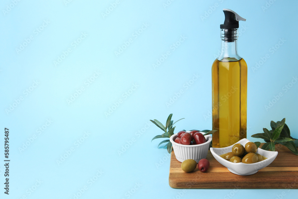 Bottle of oil, olives and tree twigs on light blue background, space for text Bottle of oil, olives and tree twigs on light blue background, space for text