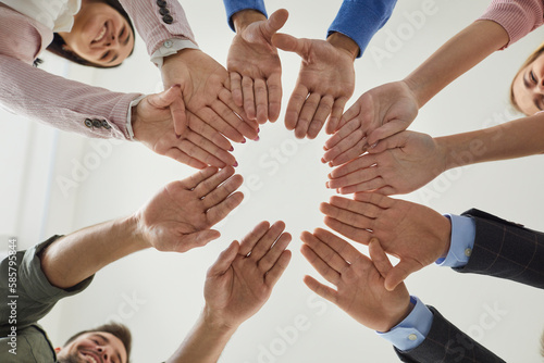 Team of business people or corporate employees join their hands. Group of happy young men and women putting their hands together, cropped shot from below. Teamwork, community, help, support concept