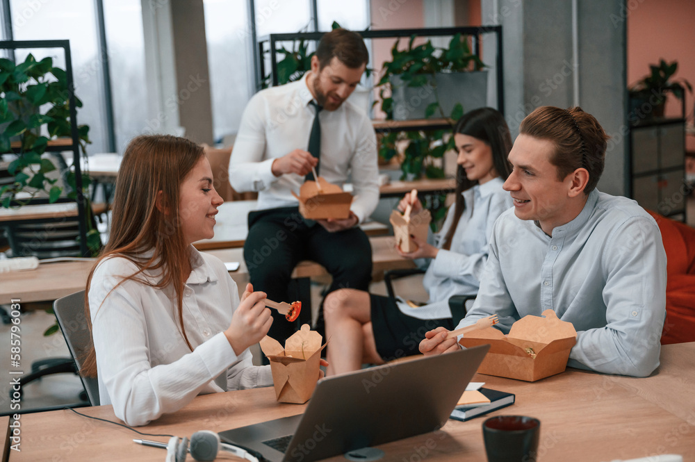 Talking, having a break. Group of coworkers are eating food from eco boxes in the office together Talking, having a break. Group of coworkers are eating food from eco boxes in the office together