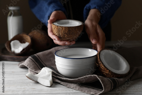Woman holding nut with coconut milk at white wooden table, closeup