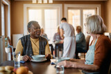 Happy black man talks to female friend while having lunch in nursing home.