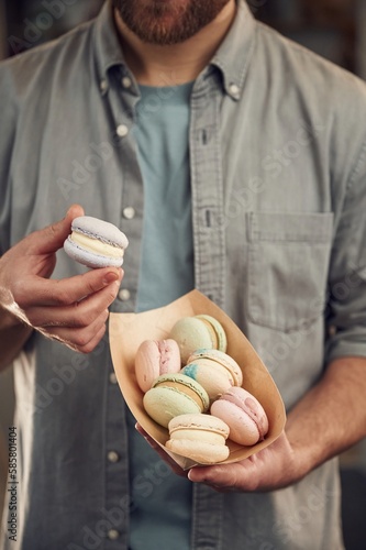 Obraz na plátně Man in casual clothes is holding macarons that are in the paper eco box