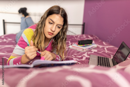 Teen schoolgirl studying at home, using laptop. Caucasian girl lying on bed and doing school homework. Distance learning online education.