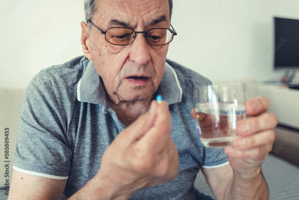 Elderly man taking pills for depression sitting on couch. Old upset patient swallowing pill with glass of water. Elderly man taking pills for depression sitting on couch. Old upset patient swallowing pill with glass of water.