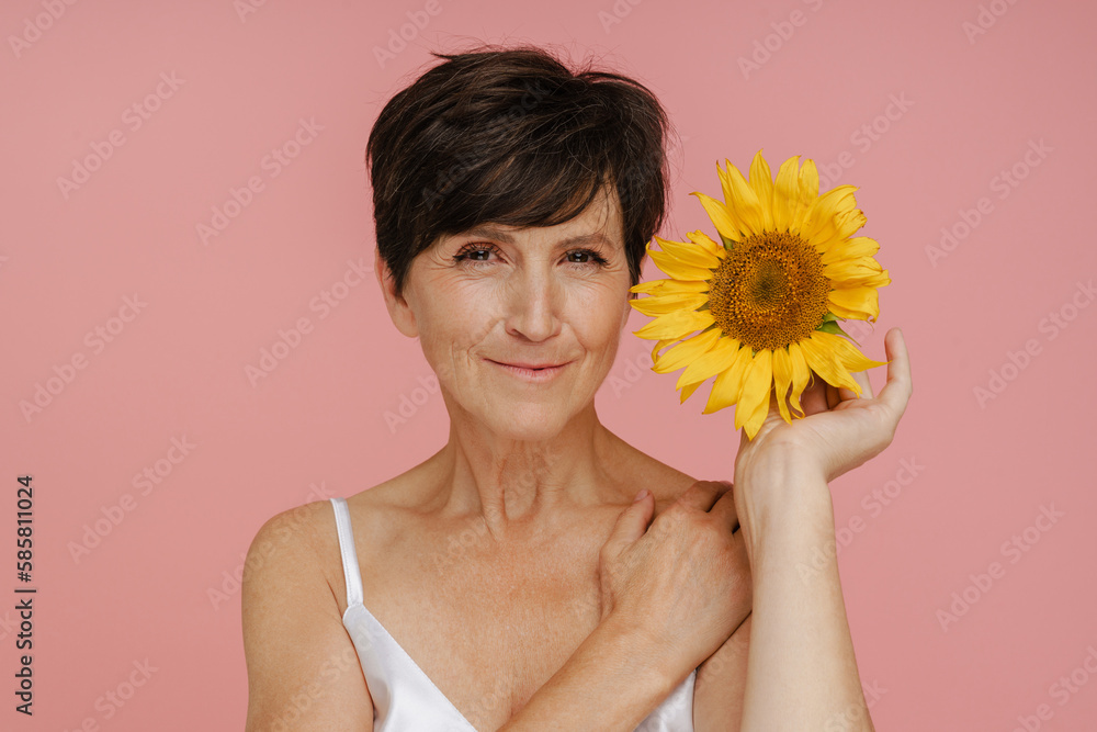 Beautiful woman smiling while posing with sunflower isolated over pink background